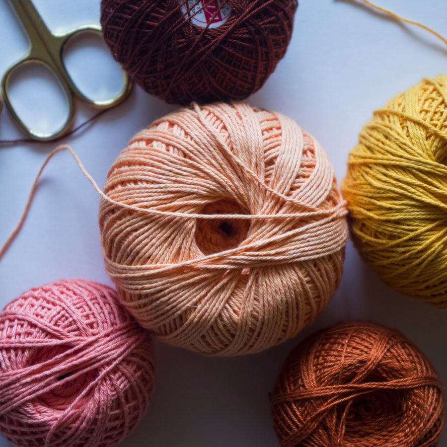 Cotton yarn in peach, pink and yellow laid out beside gold scissors